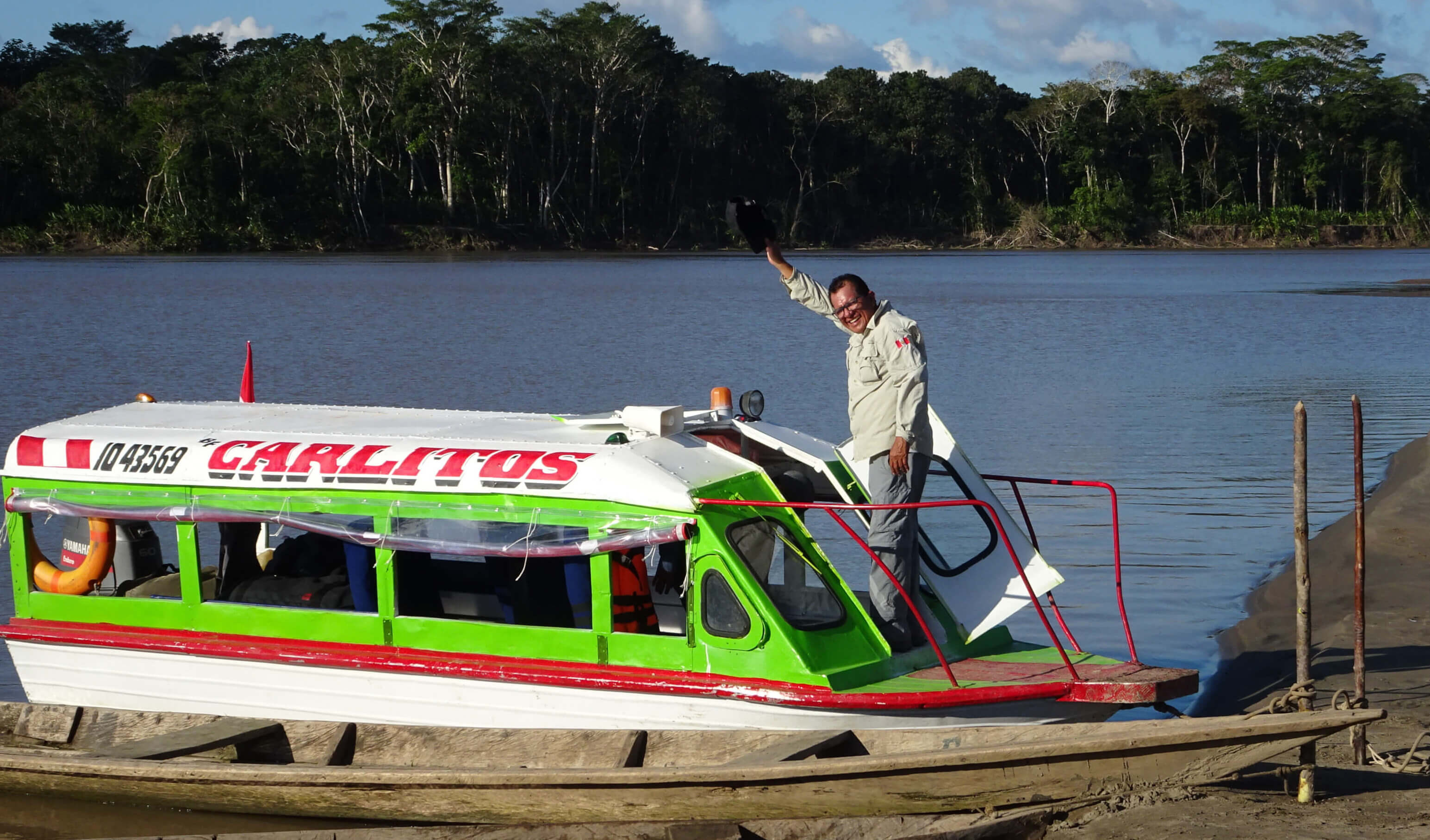 A guide is waving from the bow of the boat docked on a beach.